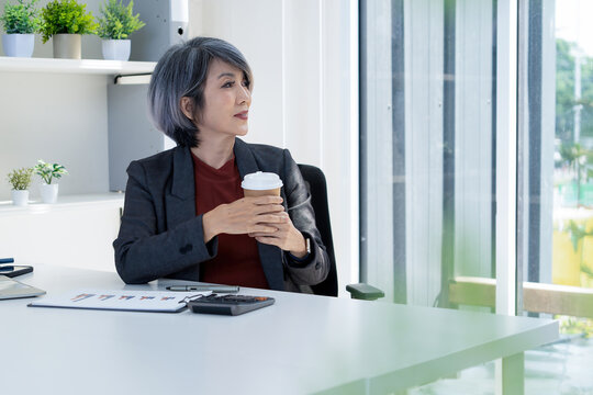 Businesswoman Taking a Coffee Break and Looking Out Window in Office