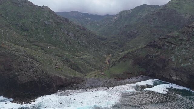 Aerial drone push in shot of the rugged coastline and green mountains leading to Playa de Tamadite beach on Tenerife, Canary Islands. Capturing remote nature and the Atlantic ocean.