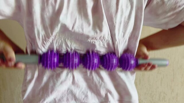 Woman massaging her back with a purple spiky ball roller stick for pain relief and muscle recovery, focusing on self care, wellness, and home physiotherapy treatment