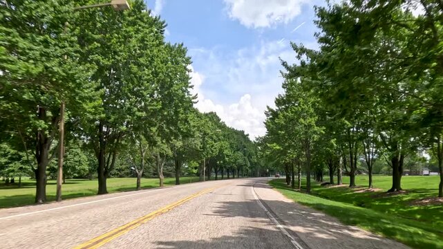 Driving POV Along Tree-Lined Campus Ring Road. Motion shot from a vehicle driving down a paved campus ring road surrounded by mature trees. Captured at University of Illinois Springfield.