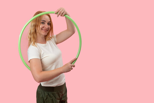 Young woman confidently holding a green hula hoop, showcasing a healthy lifestyle, fitness, and active living against a vibrant pink background