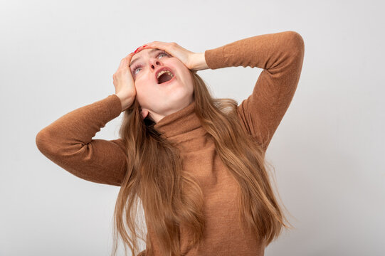 Young woman clutching her head and screaming in a studio portrait, conveying intense stress, anxiety and despair as she struggles with overwhelming emotions and mental distress