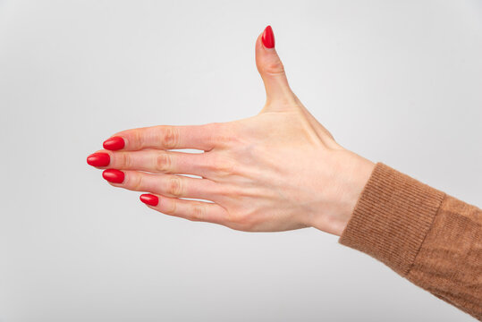 Female hand with red polished nails forming a pointed hand gesture, symbolizing communication, authority, or a playful gun sign against a neutral background