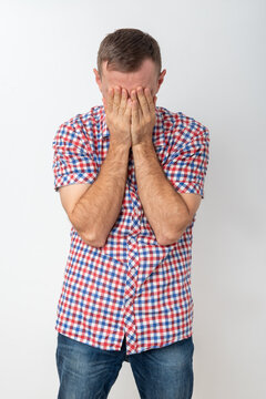 Upset young man with head in hands, covering his face in distress on a plain background, conveying sadness, frustration, shame and emotional overwhelm