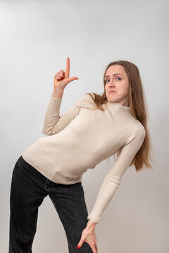 Young woman with long hair making an L hand sign on white background, showing disappointment, sarcasm and defeatful mockeryexpression of frustration, displeasure and loss