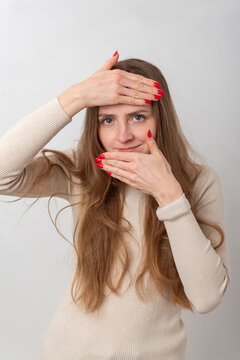 Woman standing against white background, framing her happy smiling face with hands into a square shape, looking at the camera with red nails and light long hair