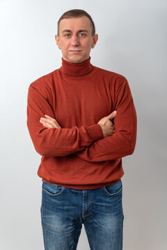 Confident man with arms crossed looking at viewer in a warm turtleneck and blue jeans, studio portrait conveying casual professionalism, approachability, and calm authority