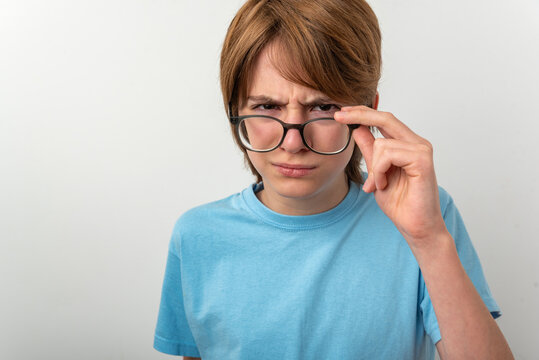 Young boy with ginger hair and a serious, questioning expression, intently looking forward while pulling down his clear rimmed glasses, focusing on a problem or challenge