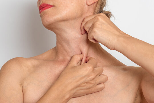 Woman touches neck and collarbone area with both hands, checking skin and lymph node area, neck muscles.