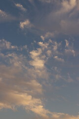 Obraz premium Clouds floating across a blue sky with hints of orange and pink hues, suggesting either sunrise or sunset
