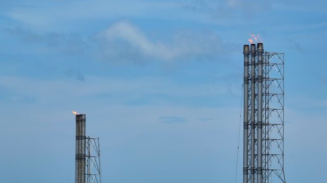 Wide aerial shot of gas flare towers at an energy facility, representing industrial safety venting, pressure relief systems, fossil fuel operations, the global shift toward cleaner energy solutions.
