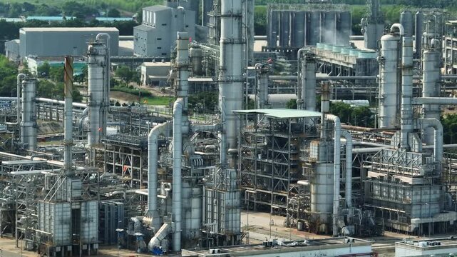 Aerial view of a coastal petrochemical industrial estate featuring distillation towers, processing units, global supply chain infrastructure supporting energy production, industrial transformation.
