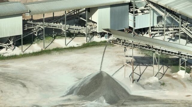 Industrial aerial view of a stone crushing facility with conveyor equipment creating aggregate piles, showcasing continuous production, heavy machinery performance, material supply chain efficiency.