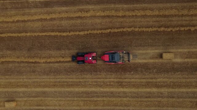 Aerial view of red square baler machinery baling straw on farmland after harvest