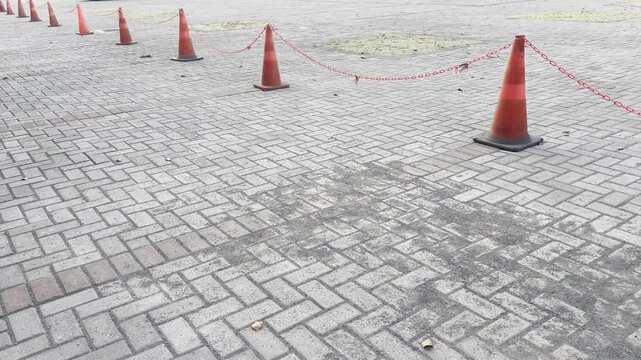 Row of orange traffic cones with chain on interlocking paving block street