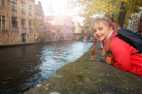 Girl with backpack leans on canal wall in autumn city