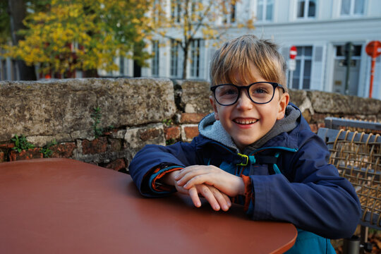 Smiling child with glasses sits at outdoor cafe table in town