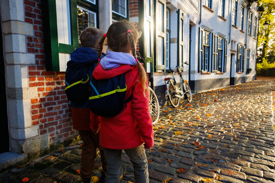 Two children with backpacks walking along cobblestone street