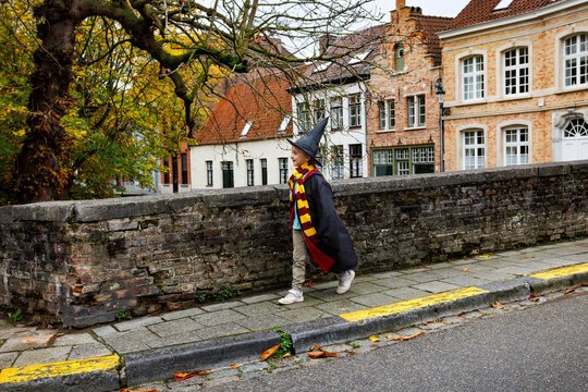 Child in wizard costume walking along brick street wall