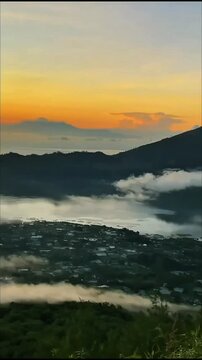 Hiker walks grassy mountain path toward glowing twin peaks above golden cloud sea, soft sunset light warms wide peaceful landscape