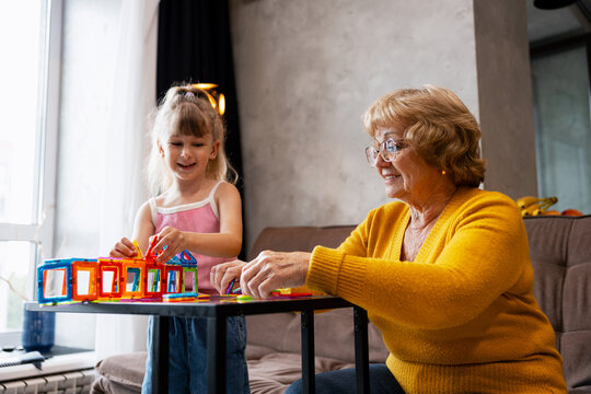 Granddaughter and grandmother playing with colorful magnetic blocks