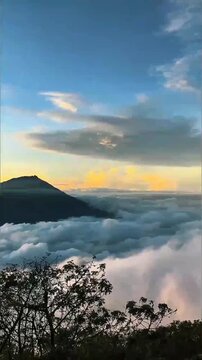 Warm golden sunset sky glows over dark mountain ridges, mist drifts across valleys and small settlements, calm soft light fills the view