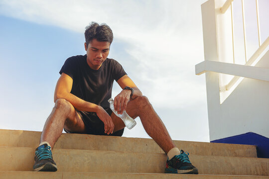 Tired runner man with a bottle of electrolyte drink freshness after training outdoor workout at the stadium stairway.