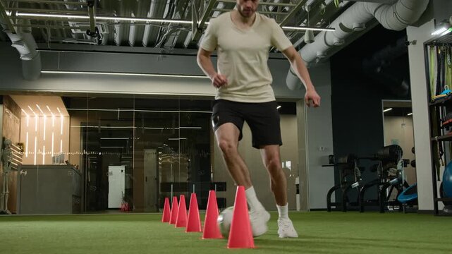 Caucasian footballer male man player dribbling ball between cones on field soccer athlete sportsman running fast energy feint moves intense training workout agility speed exercise game preparation