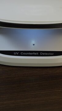 Examination of Thai baht (THB) cash money with UV counterfeit detector. Concept of authenticity check, fight against counterfeiting of banknotes, anti fraud measures in Thailand. Close up view.