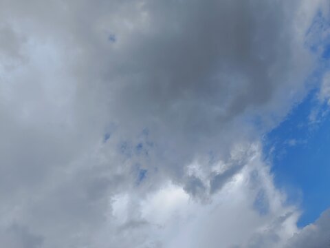Large mass of gray clouds against a bright blue sky. Contrasting partly cloudy weather background. Atmospheric texture