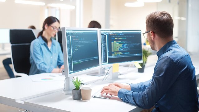 Young Caucasian IT programer working on desktop computers in data center control room. Professional man worker writing on sophisticated programming code language in modern office. Internet technology