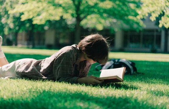 A student enjoying a peaceful moment on lush green grass fully absorbed in reading a book outside on campus embracing a journey of self study and personal growth