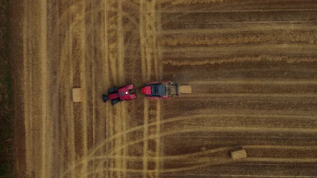 Aerial view of red square baler machinery baling straw on farmland after harvest