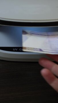 Examination of Uzbekistan Sum (UZS) cash money with UV counterfeit detector. Concept of authenticity check, fight against counterfeiting of banknotes, anti fraud measures in Uzbekistan. Close up view.
