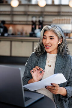 Woman on video call with documents in cafe.