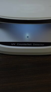 Examination of Uzbekistan Sum (UZS) cash money with UV counterfeit detector. Concept of authenticity check, fight against counterfeiting of banknotes, anti fraud measures in Uzbekistan. Close up view.