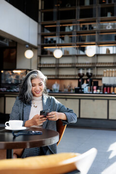 Woman smiles at mobile phone in cafe with coffee.