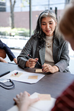 Woman leads meeting, writing on sticky notes.