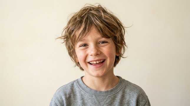 A young boy with curly hair smiling and wearing a gray sweatshirt.