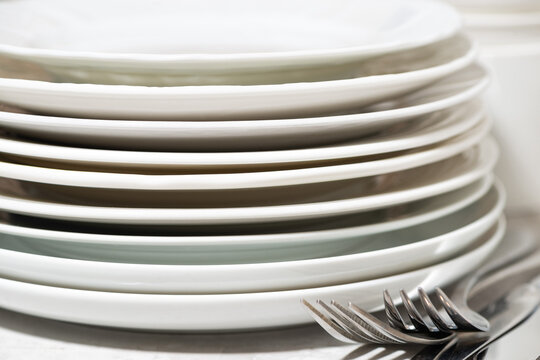 stack of clean plates and cutlery on white table