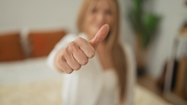 Woman young blonde on bed showing thumb down gesture in studio, closeup of extended thumb and alternating thumbs up to thumbs down sequence; mixed reaction ambivalence.