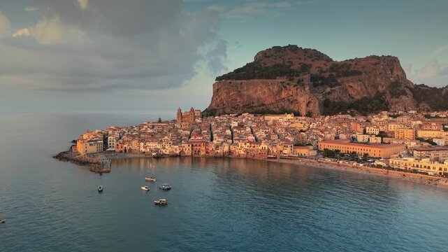 Aerial view of Cefalu seaside town with sandy beach and rocky coastline. Iconic cathedral and giant cliff dominate picturesque Italian bay. Cefalu, Sicily, Italy. Cefalu resort city nestled below La R