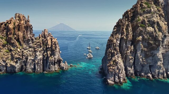 Flying over crystal clear turquoise sea water near Panarea and Basiluzzo rocks. cenic coastal landscape of Aeolian islands, Sicily, Italy. Catamarans anchored near cliffs of Basiluzzo