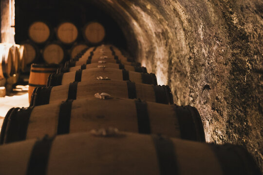 Rows of wooden barrels line a stone tunnel in a wine cellar, capturing the traditional process of aging and fermentation.