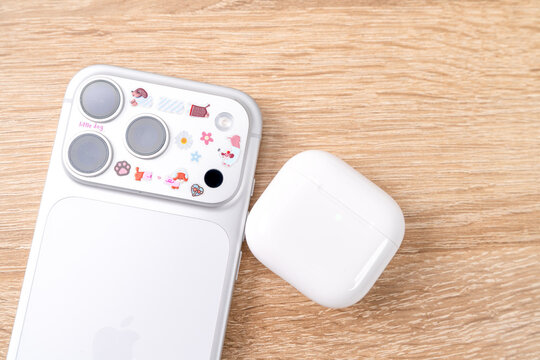 Bar, Montenegro: February 6, 2026: Overhead view of white apple iphone 17 pro with stickers and wireless earbuds case on warm wooden surface, new technology delivery flatlay concept