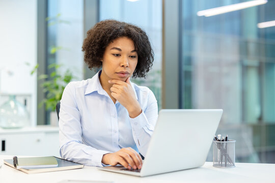 Serious and focused young African American woman sitting at a desk in the office and working on a laptop
