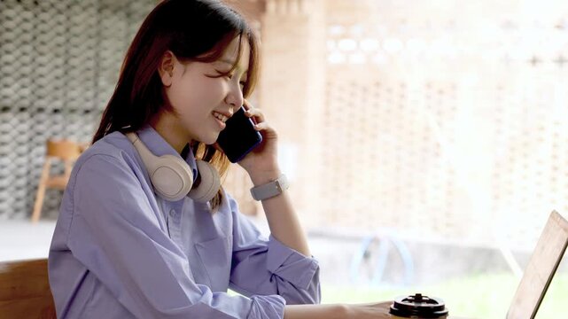 Young Asian Businesswoman Working Remotely with Laptop and Smartphone in Traditional Wooden Cafe, Digital Nomad Lifestyle