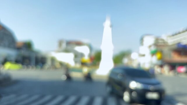 Tugu yogyakarta monument amidst bustling street traffic, with a blurry urban backdrop and clear blue sky. Ideal for travel content.