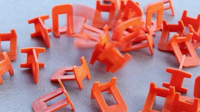 Orange plastic clamps for tile leveling system, close-up. Professional consumables for laying ceramic and porcelain tiles. A large number of orange plastic clamps fall on a gray surface. Repair