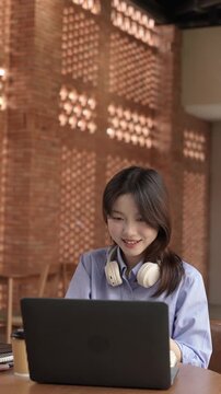 Young Asian Businesswoman Working Remotely with Laptop and Smartphone in Traditional Wooden Cafe, Digital Nomad Lifestyle